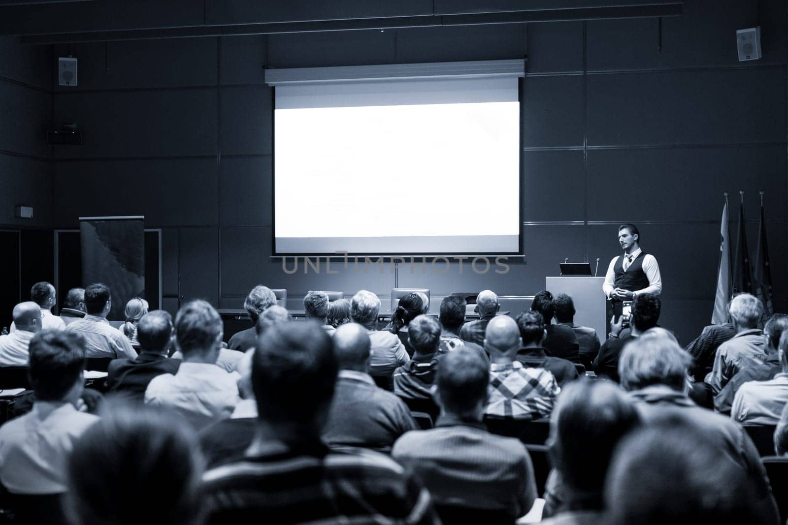 Speaker Giving a Talk at Business Meeting. Audience in the conference hall. Business and Entrepreneurship concept. Black and white blue toned image.