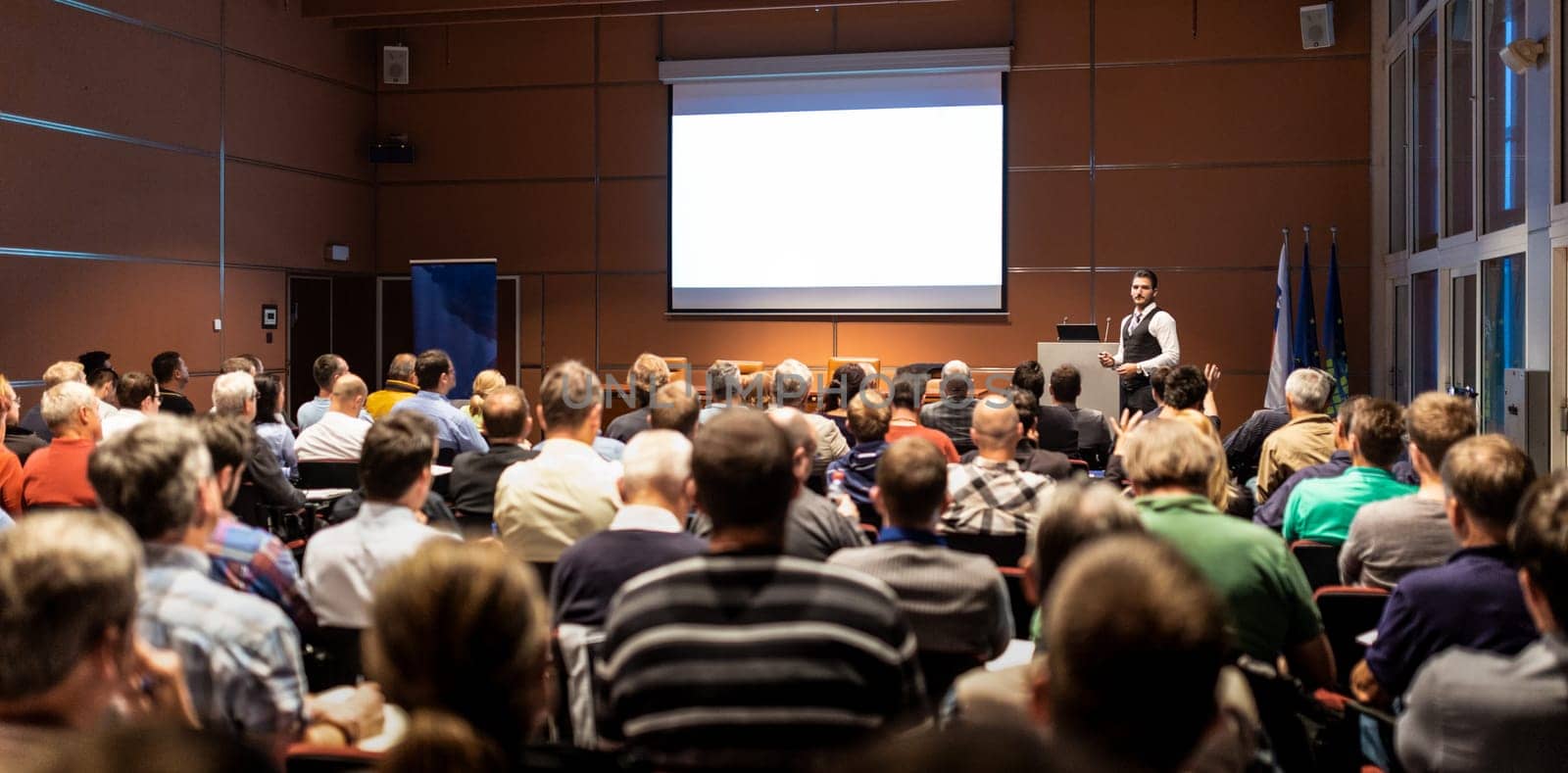 Speaker giving a talk in conference hall at business meeting event. Rear view of unrecognizable people in audience at the conference hall. Business and entrepreneurship concept.