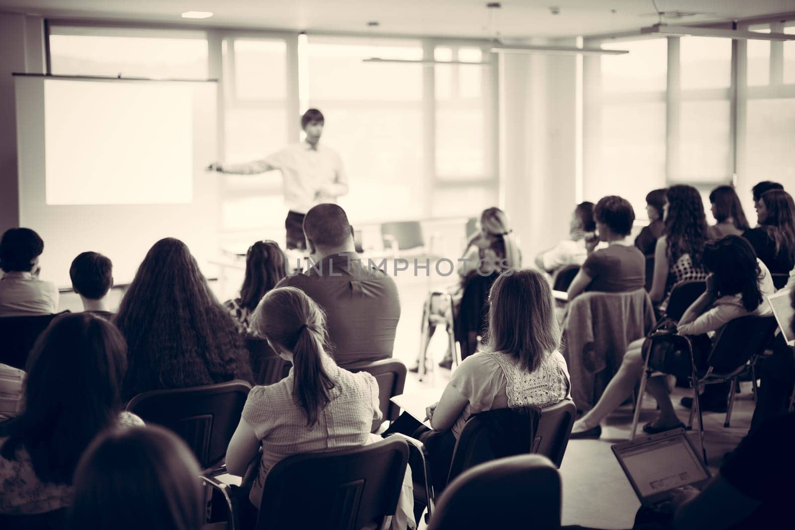Business and entrepreneurship symposium. Speaker giving a talk at business meeting. Audience in conference hall. Rear view of unrecognized participant in audience.