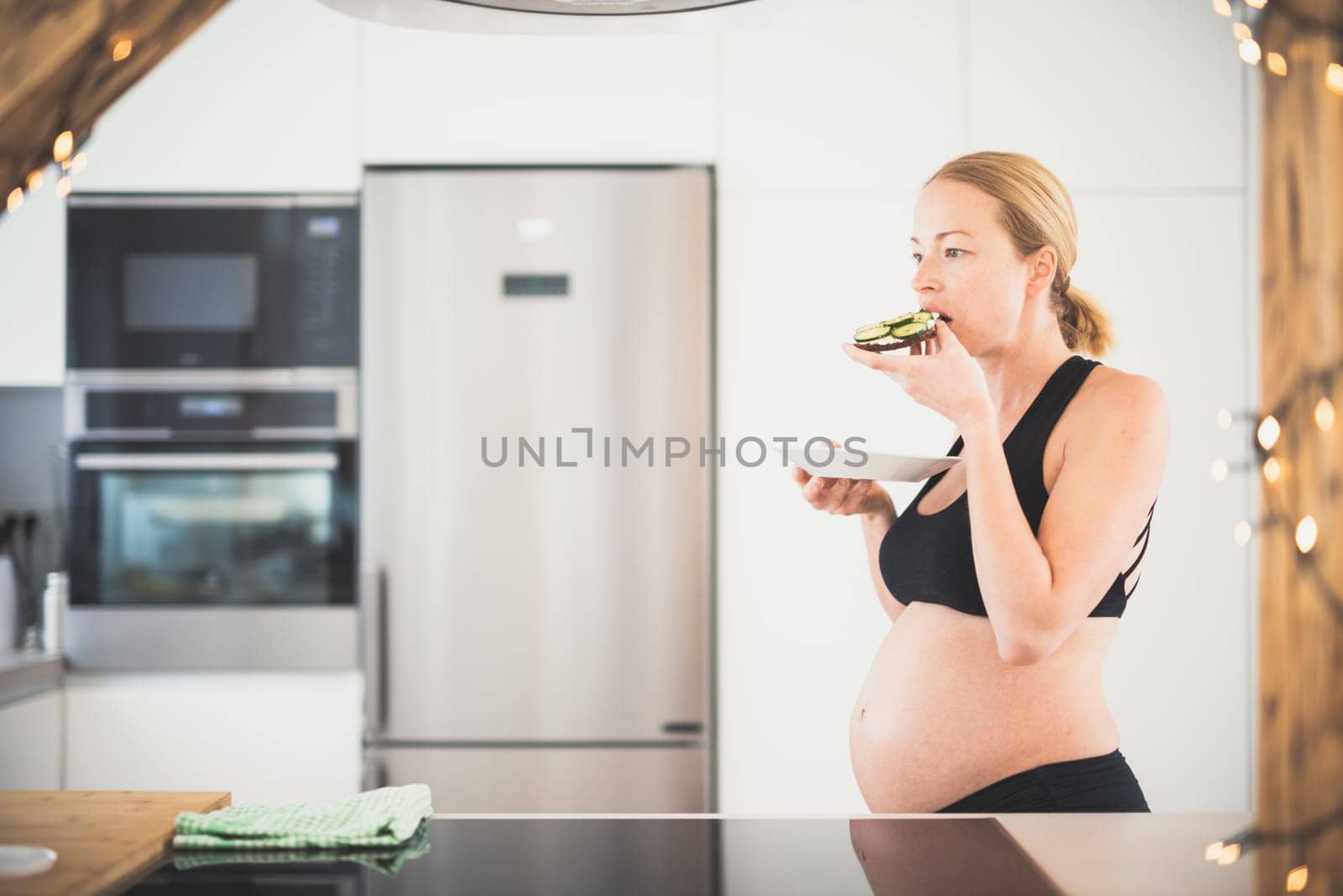 Beautiful sporty fit young pregnant woman having a healthy snack in home kitchen. Healty lifestyle concept