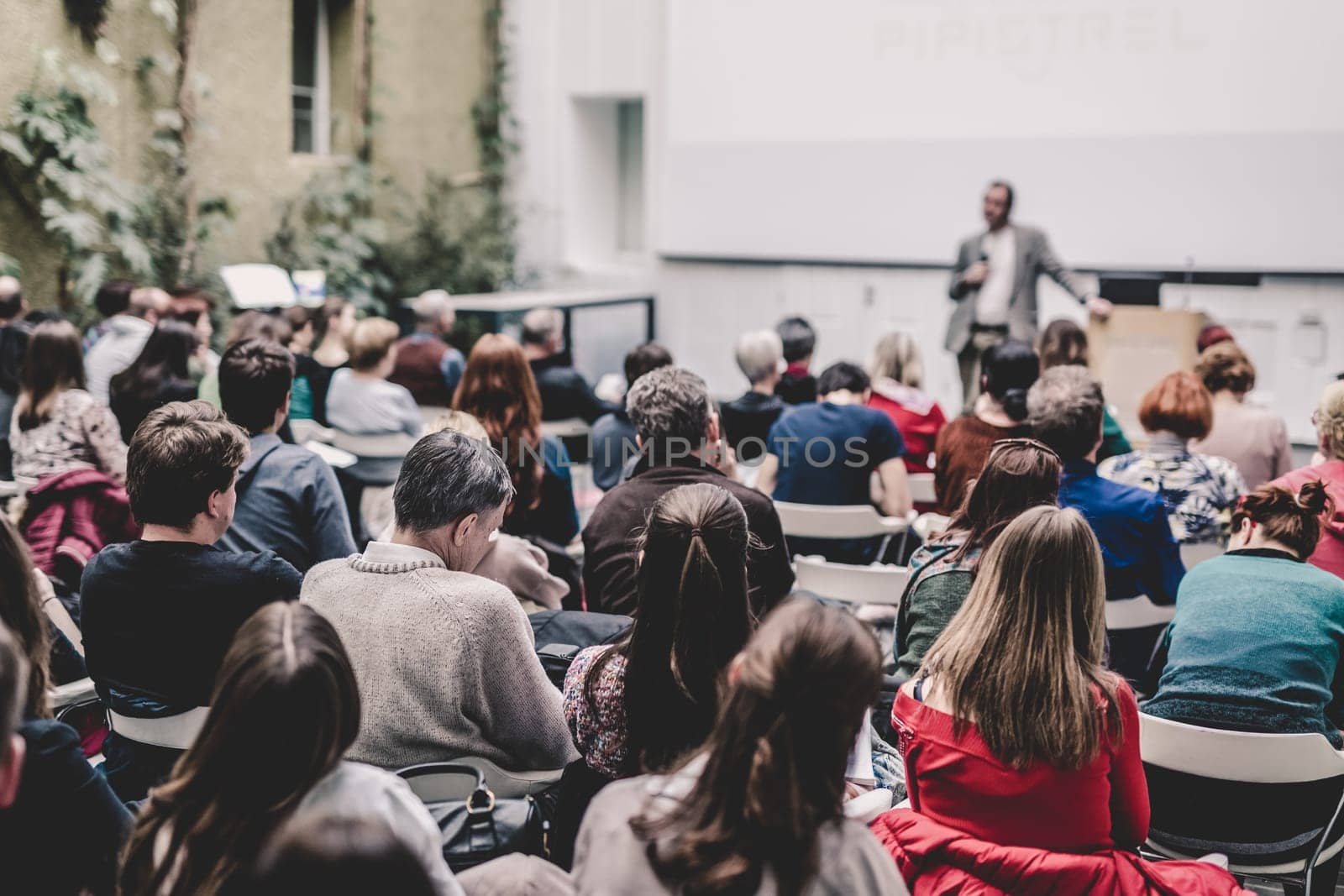 Male speaker giving presentation in lecture hall at university workshop. Audience in conference hall. Rear view of unrecognized participant. Scientific conference event. Copy space on whitescreen.