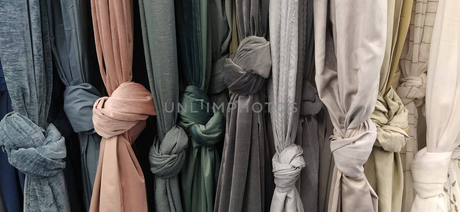 Curtain and fabric for drapery and interior decoration. Samples of fabrics in the store are hung vertically and tied in knots. White, gray, green, peach, champagne and yellow curtains in the showcase