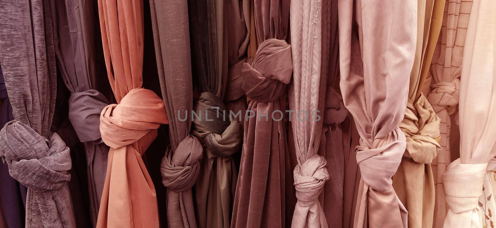Curtain and fabric for drapery and interior decoration. Samples of fabrics in the store are hung vertically and tied in knots. Curtains in the showcase. Curtains in pink, beige, brown warm tones