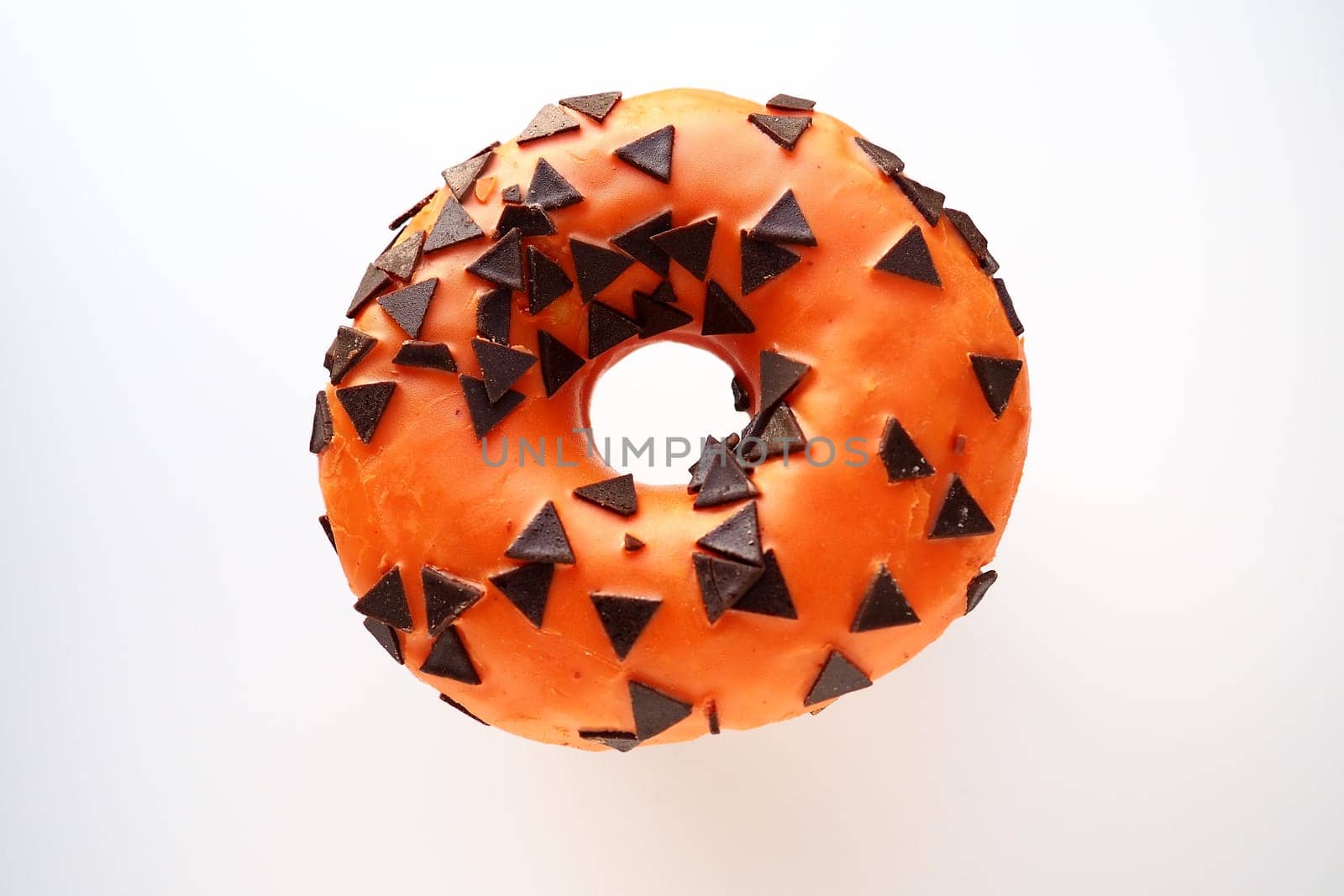 Halloween donut with orange frosting and chocolate triangles as a sweet decorative topping. Childrens holiday sweets on a white background. Trick or treat. All Hallows Eve. All Saints Eve Doughnut.