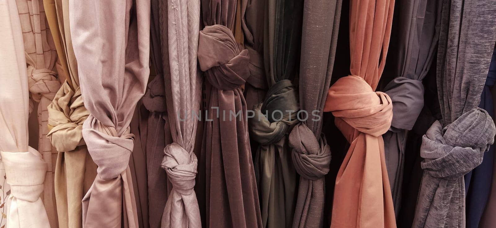 Curtain and fabric for drapery and interior decoration. Samples of fabrics in the store are hung vertically and tied in knots. Curtains in the showcase