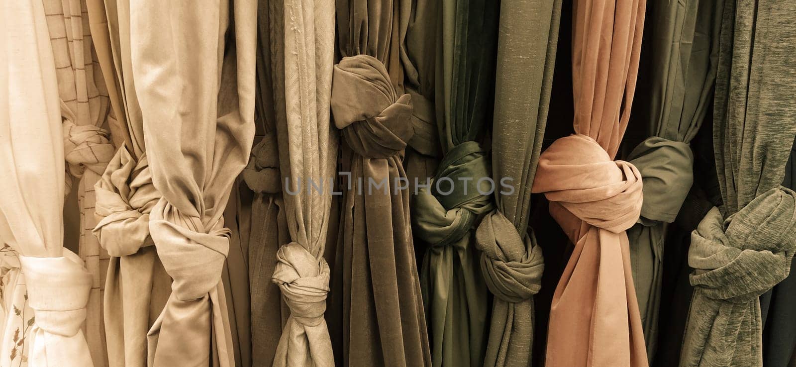Curtain and fabric for drapery and interior decoration. Samples of fabrics in the store are hung vertically and tied in knots. Curtains in the showcase. Beige, brown, gray, yellow and peach fabric