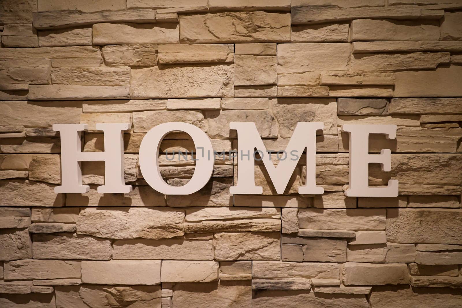 On a wall covered with narrow stones, the word "Home"" is written."