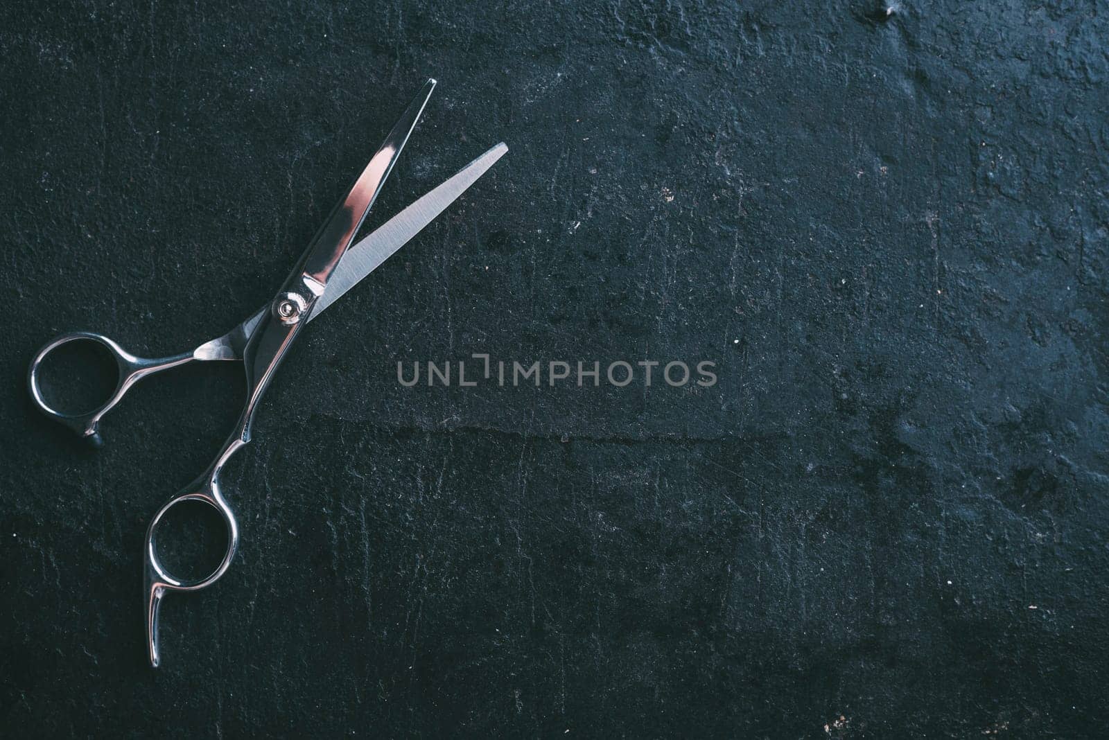 Hairdresser scissors on dark rustic background with copyspace from above. Professional hairstyle salon studio background design. Top view of haircut tool on black.