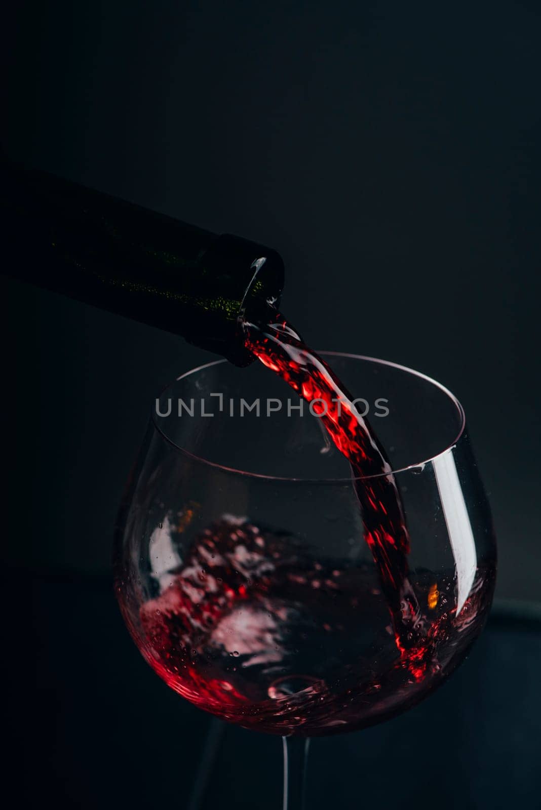 Red wine pouring in wine glass over black background. Closeup of red wine splashing in wineglass in restaurant. Wine tasting.