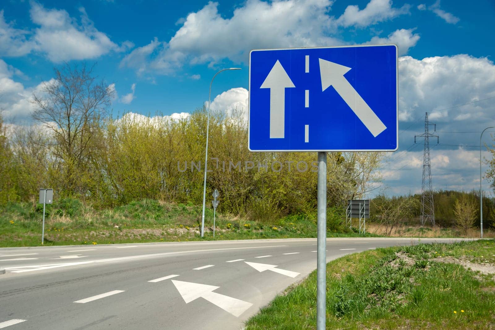 Blue rectangle road sign and white arrows, spring day