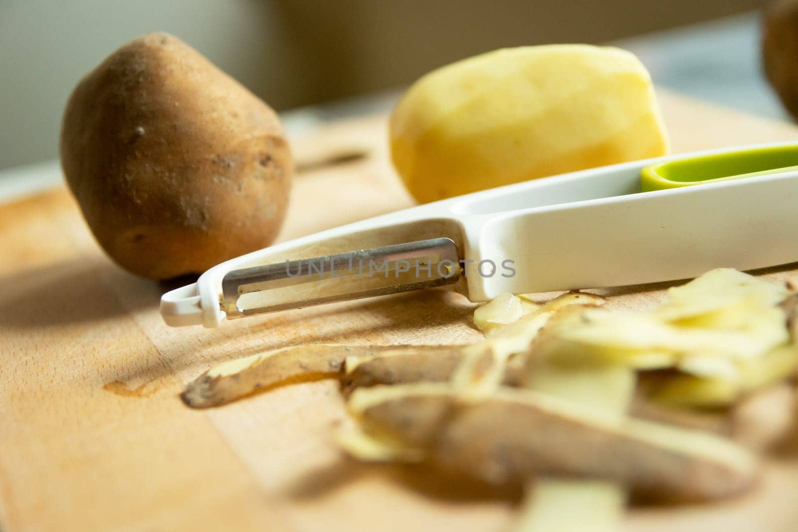 Peeler and potatoes with peelings on the wooden table
