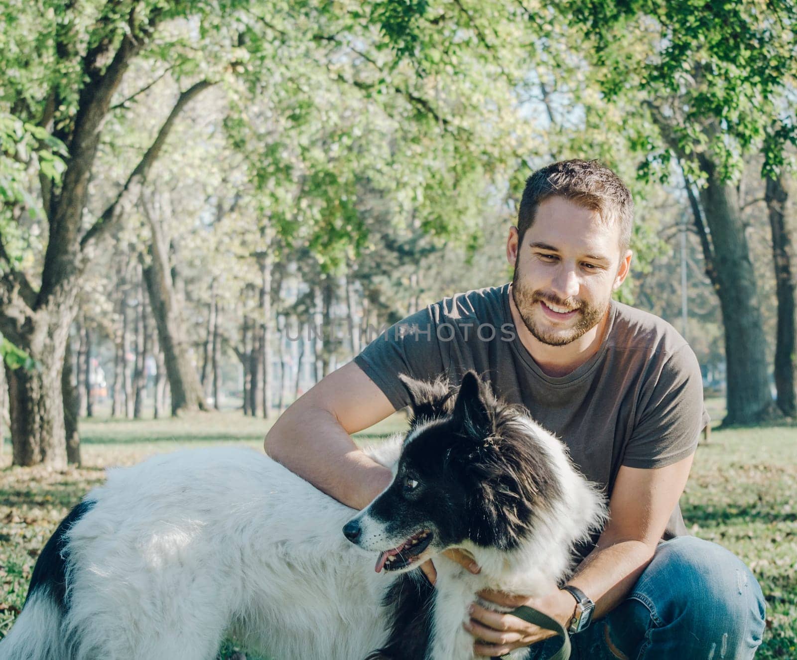 Man with his dog playing outdoor in the park. Young owner hugs his pet in nature.