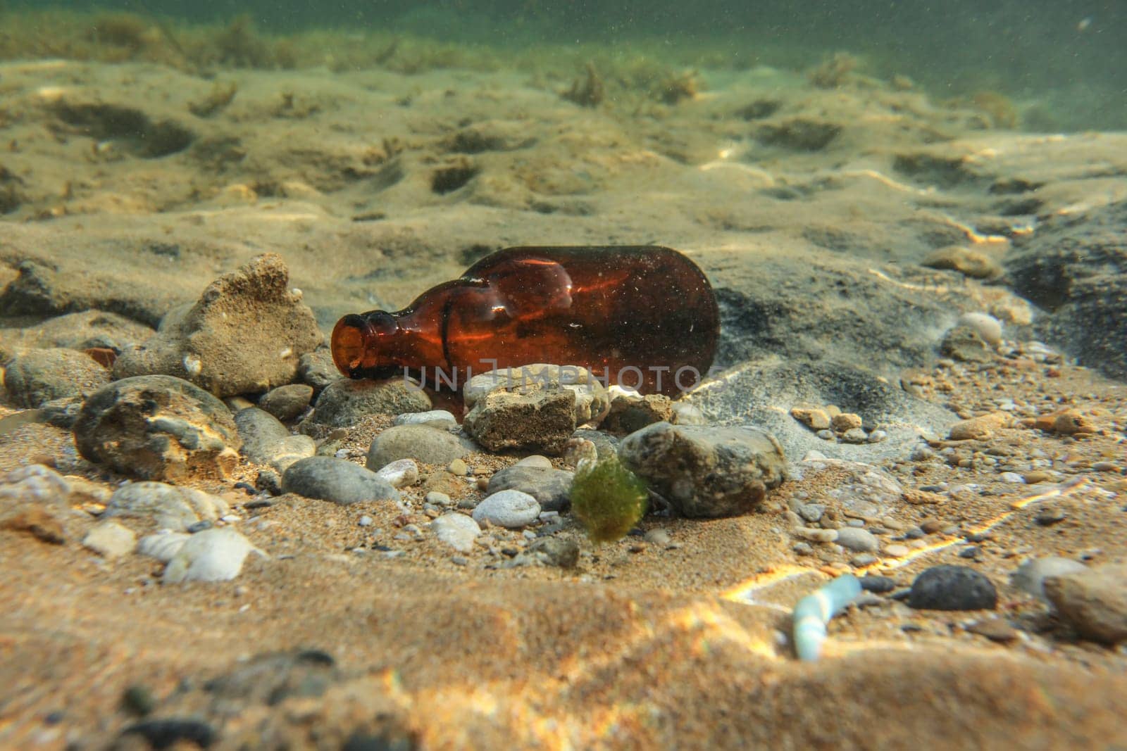 Underwater photo, discarded small beer bottle on sea floor. Ocean littering concept.