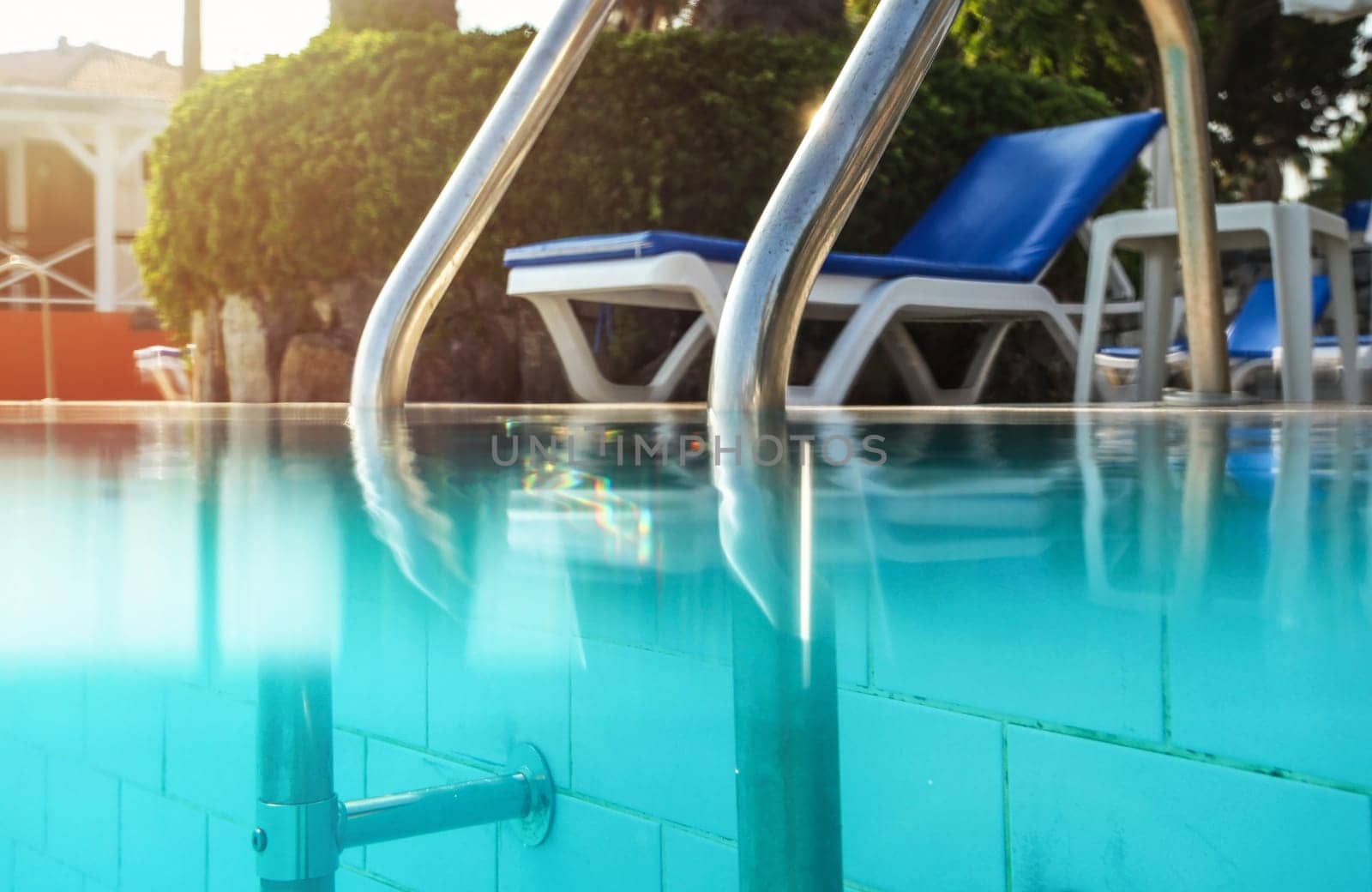 Partially underwater photo, steel handrails at entry to swimming pool, backlight sun shining in background. Vacation / relax image.