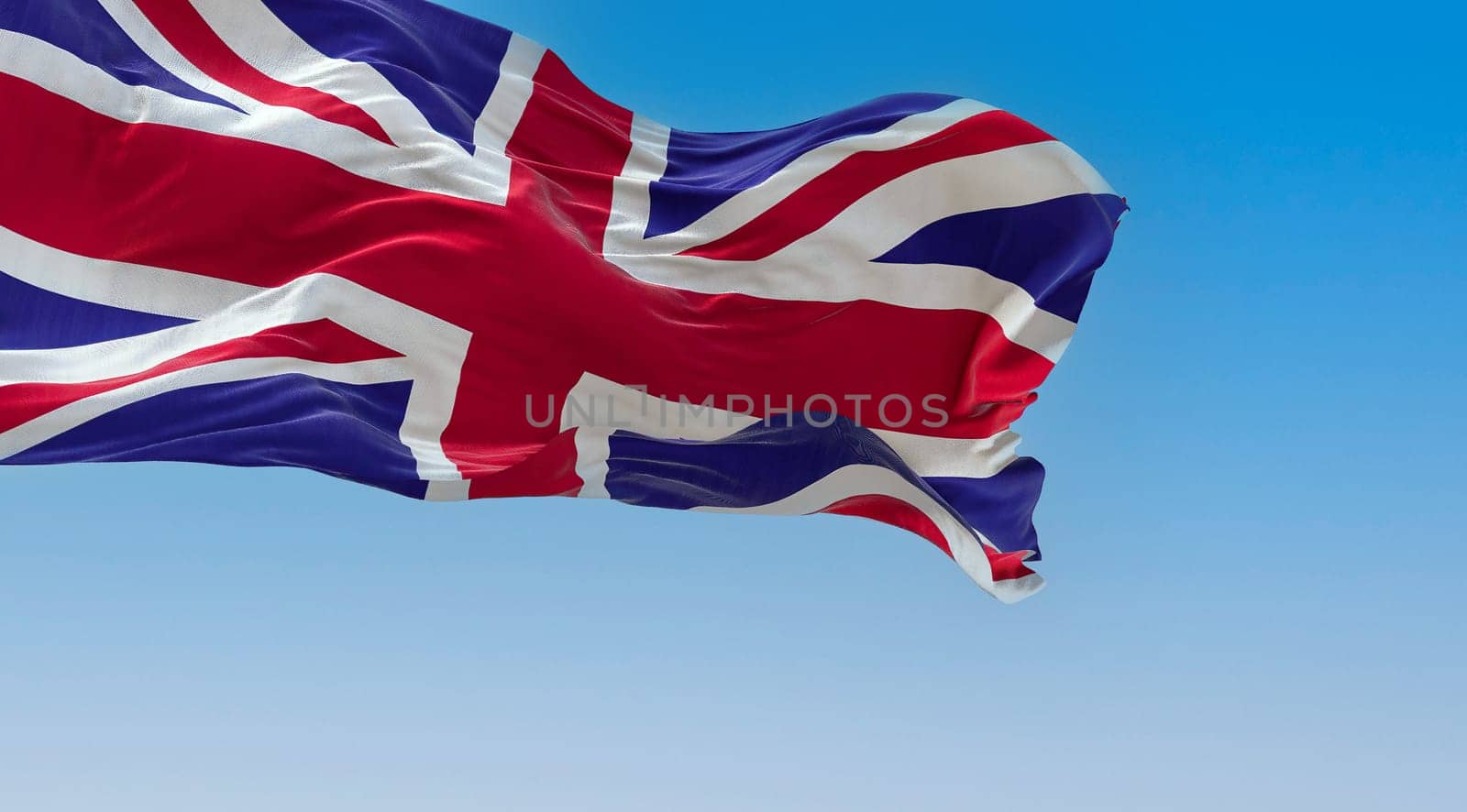 United Kingdom flag waving in the wind on a clear day. Union Jack. Blue field with red, white crosses of patron saints. Rippled fabric. Realistic 3d illustration