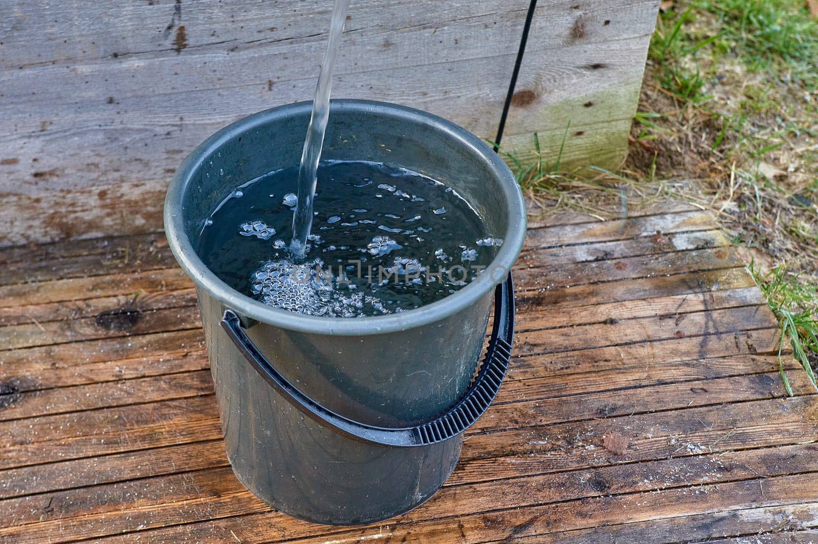 a black plastic bucket is filled with water from the pump. High quality photo