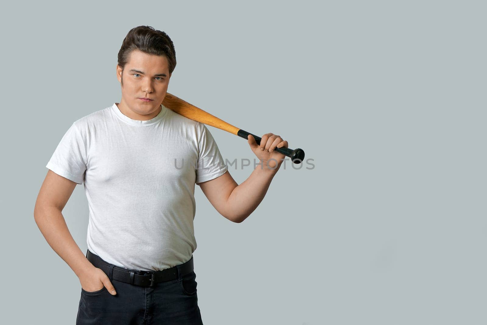 A stylish man holds a bat on his shoulder on a gray isolated background. High quality photo