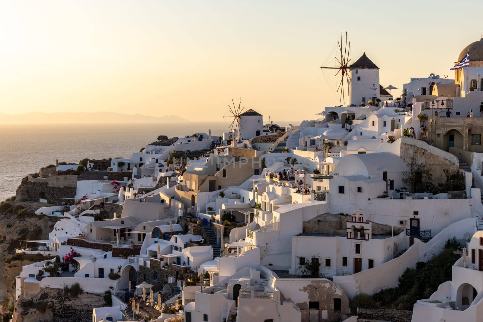 Oia, Santorini, Greece - June 28, 2021: Whitewashed houses and windmills in Oia in warm rays of sunset on Santorini island. Greece