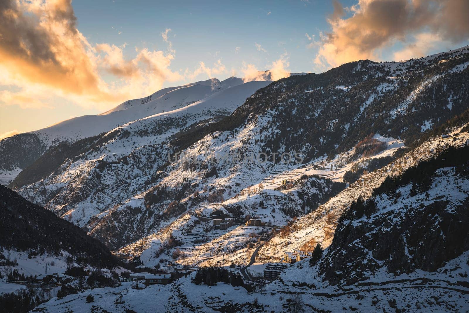 El Tarter village in a valley between mountains. Sunset light illuminating side of a mountain and clouds. Ski winter holidays, Andorra, Pyrenees