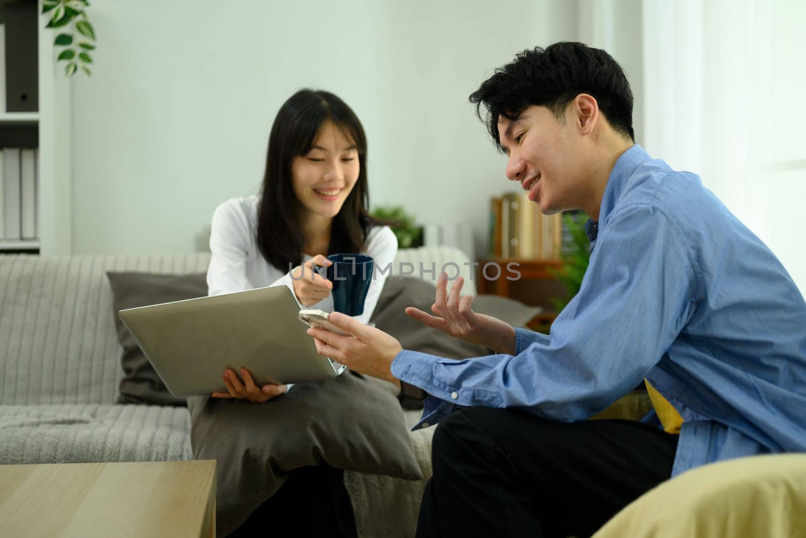 Happy young couple enjoys a conversation and using laptop in their cozy living room.