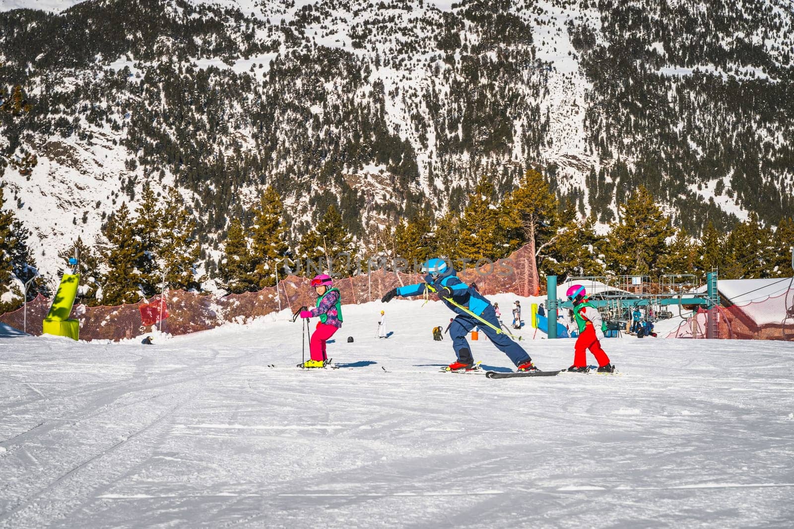 Ski instructor helping out and teaching young kids how to ski, El Tarter green slope. Winter holidays in Andorra, Pyrenees Mountains, Grandvalira