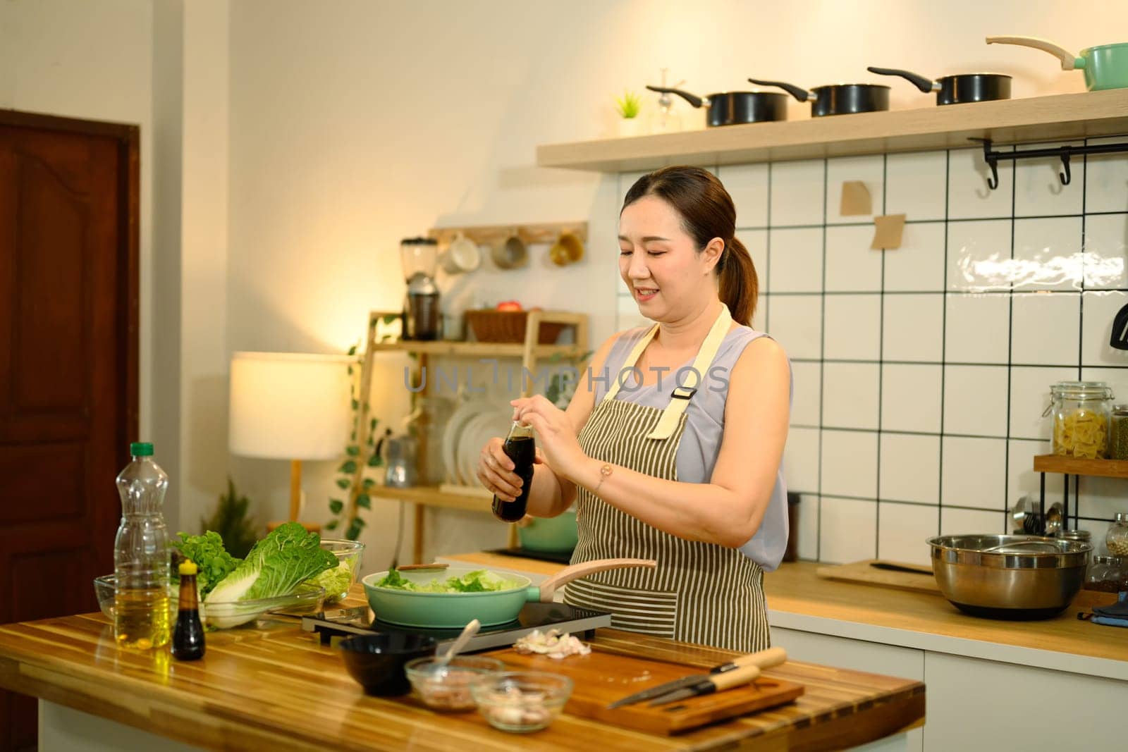 Smiling adult woman adding soy sauce into a pan with vegetables while cooking a healthy meal.