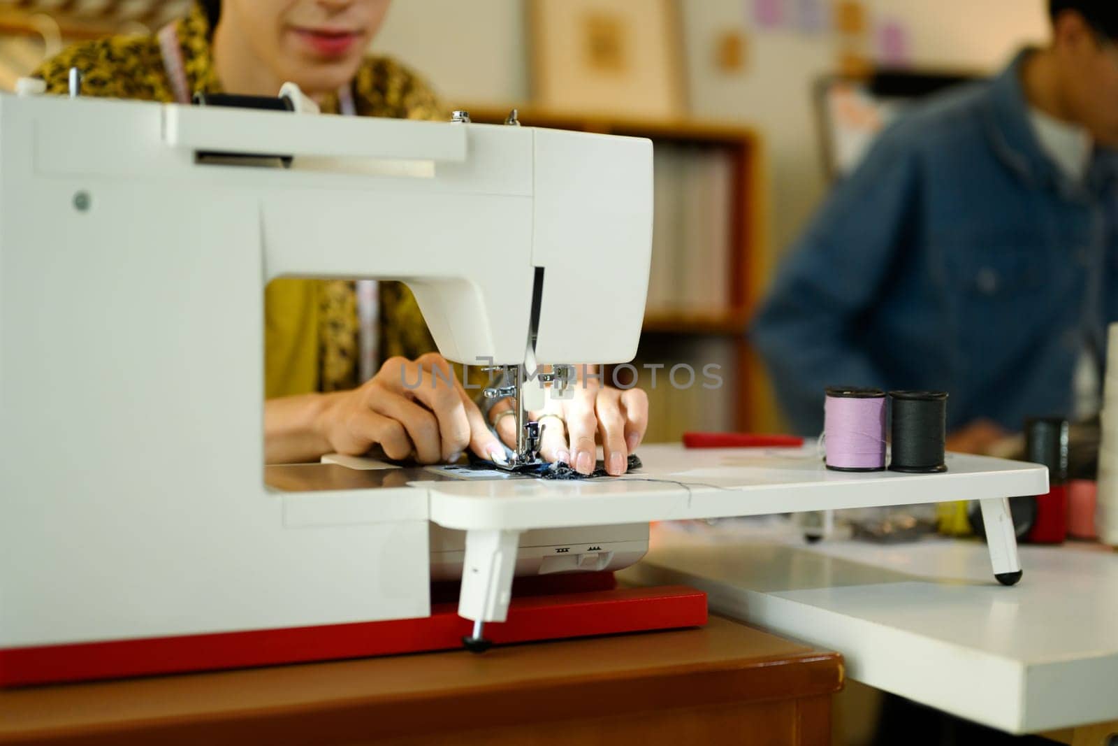 Close up of young designer or tailor working on a sewing machine in stylish studio.