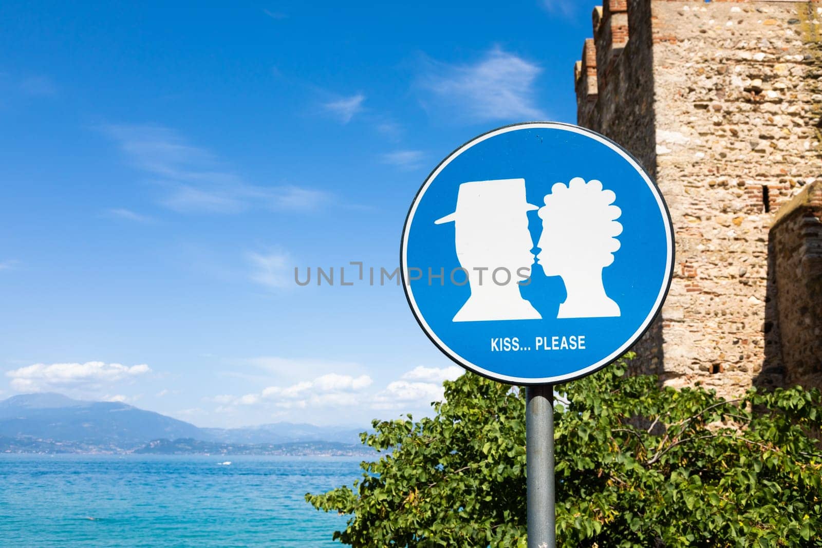 Kiss street sign located in public area in front of Sirmione castle, Italy. Concept of love, couple, romantic