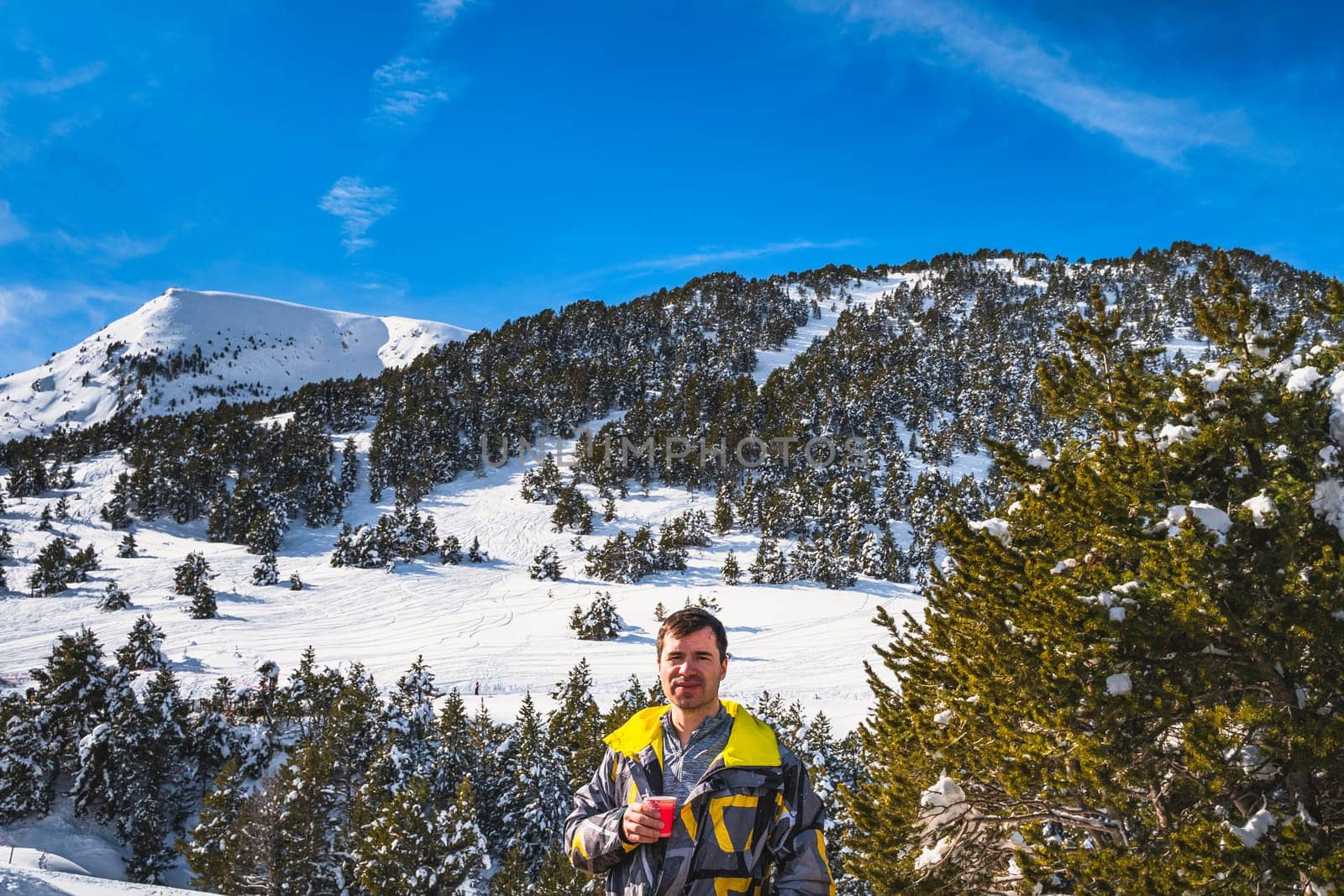 Men drinking coffee or tee, smiling and looking at camera, snowy forest and mountains in background. Winter ski holidays, Andorra, El Tarter, Pyrenees