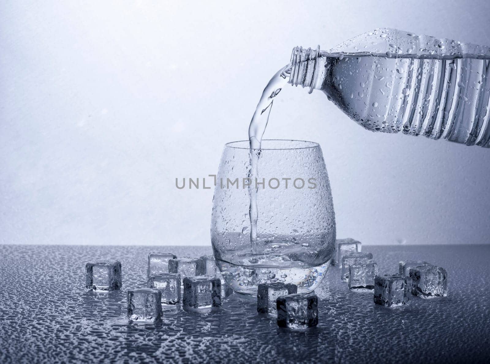 Pouring fresh drinking mineral water from plastic bottle. Glass filled with water over white background.