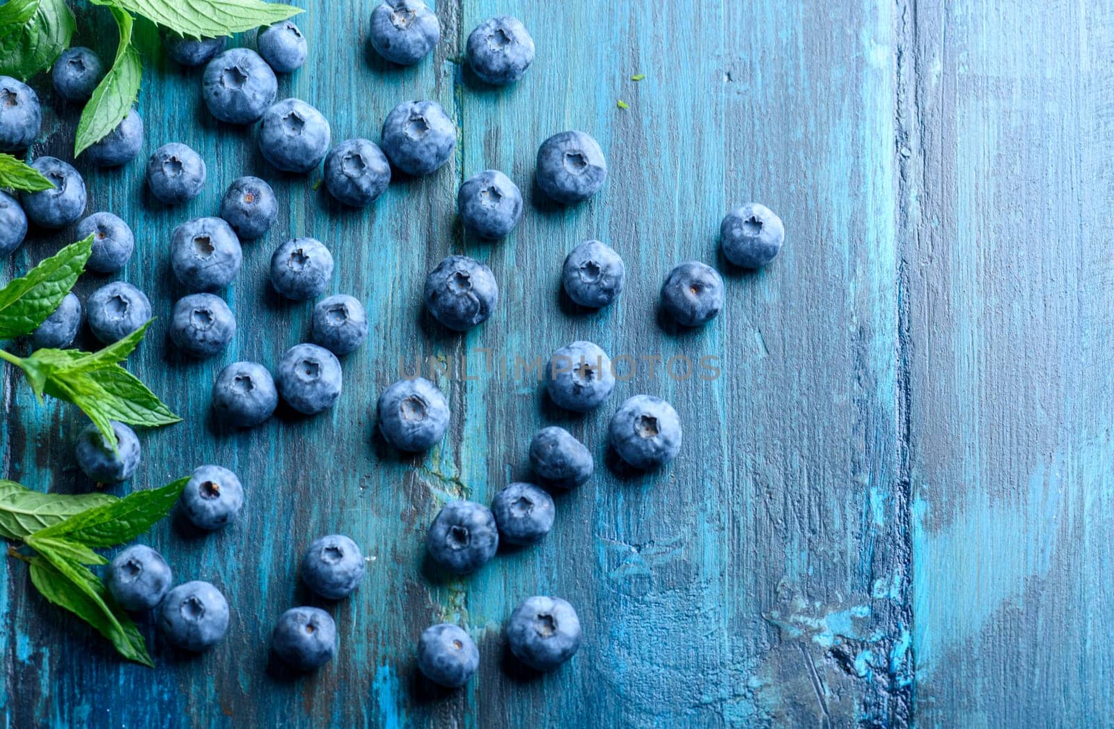 Fresh blueberries on blue rustic wooden table pattern. Healthy organic seasonal fruit background design. Organic food blueberries and mint leaf for healthy lifestyle.