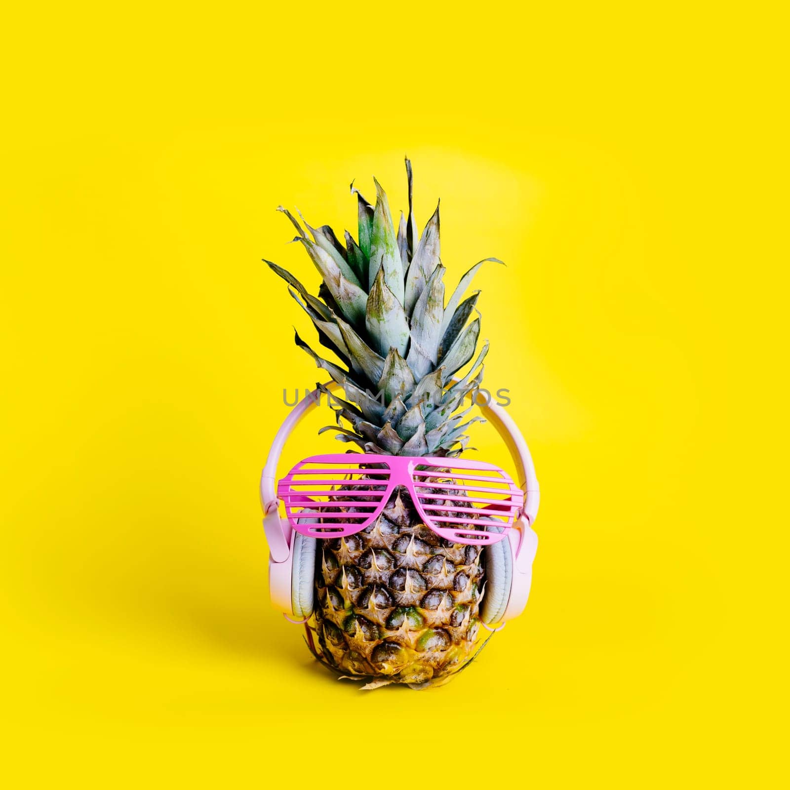 Fashionable  trendy pineapple fruit with headphones and sun glasses listen to the music over bright pastel yellow background. Cool hipster ananas with funny face. Summer holiday vacation and tropical beach party concept.