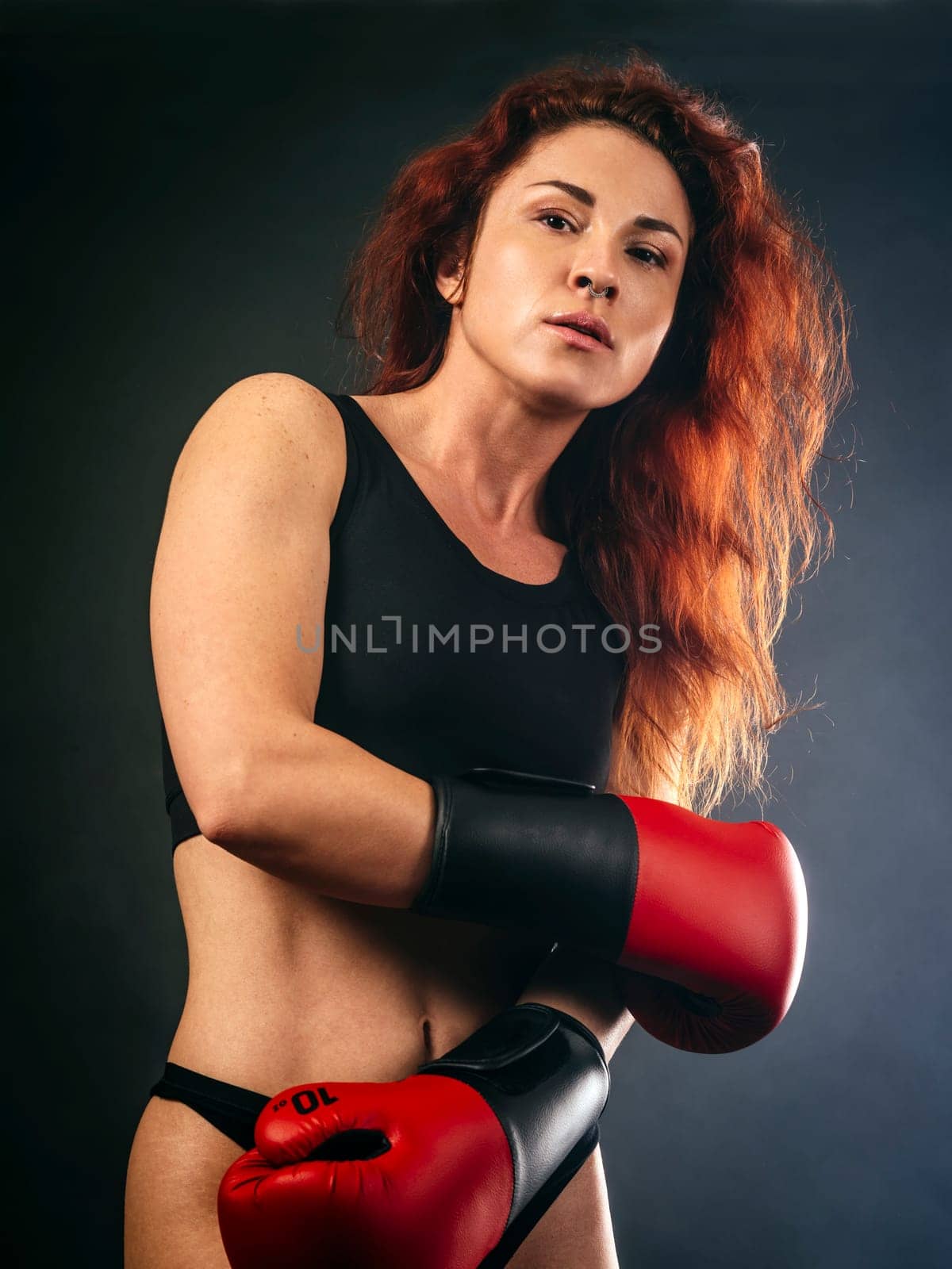 Beautiful woman with long red hair wearing boxing gloves and sportswear.