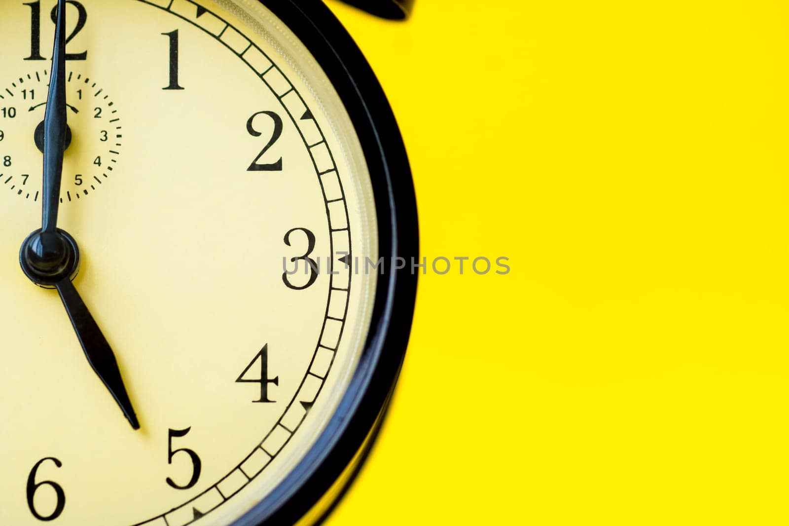 Closeup of a vintage analog black clock on a yellow background displaying 5 o'clock