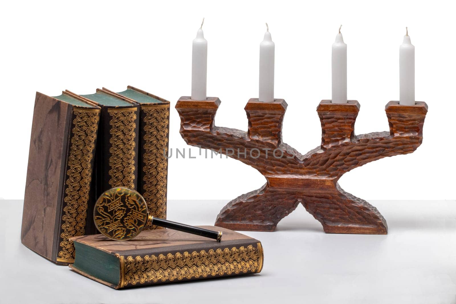 Ancient books with a magnifying glass and a antique wooden candle holder on a bright table isolated on a white background.
