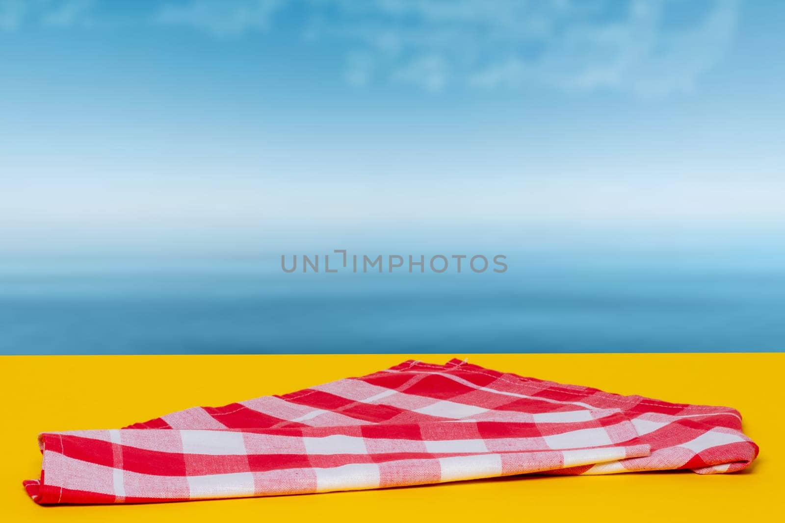 Empty table product. Empty red checkered tablecloth on yellow table over abstract blurred ocean background. Space for your food and product display montage.
