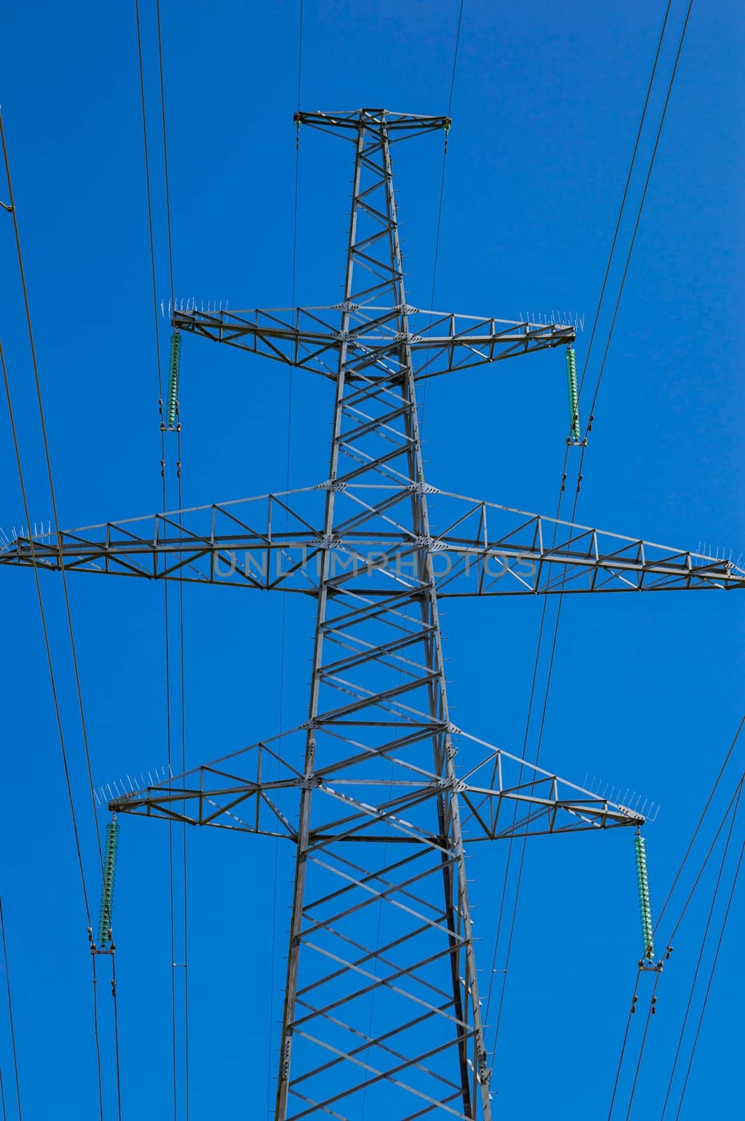 Tower with high-voltage energy transmission wires against the blue sky. High-voltage tower. Electrical wires and fuses. Energy business. Energy industry. Import and export of energy. Blue sky.