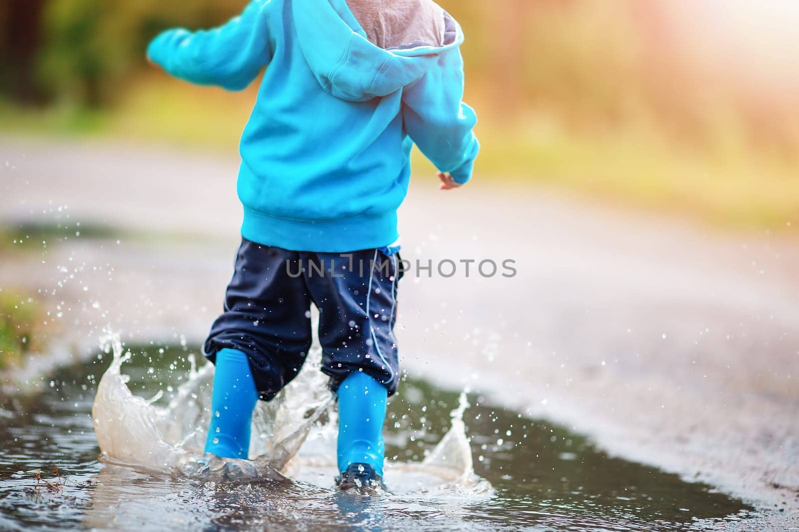 Small child jumping through puddles in nature in spring. Concept of the childhood and family relation.