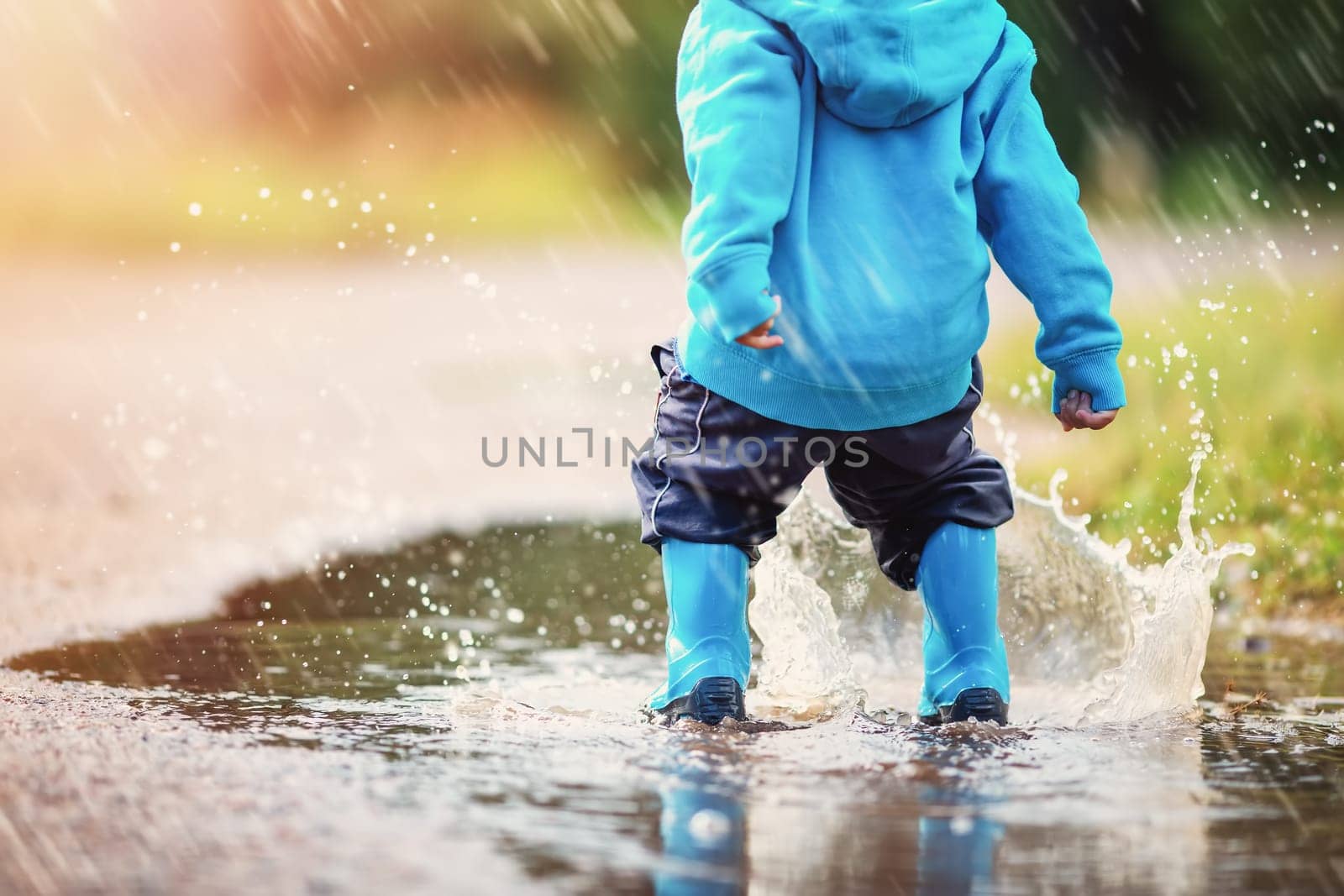 Small child jumping through puddles in nature in spring. Concept of the childhood and family relation.