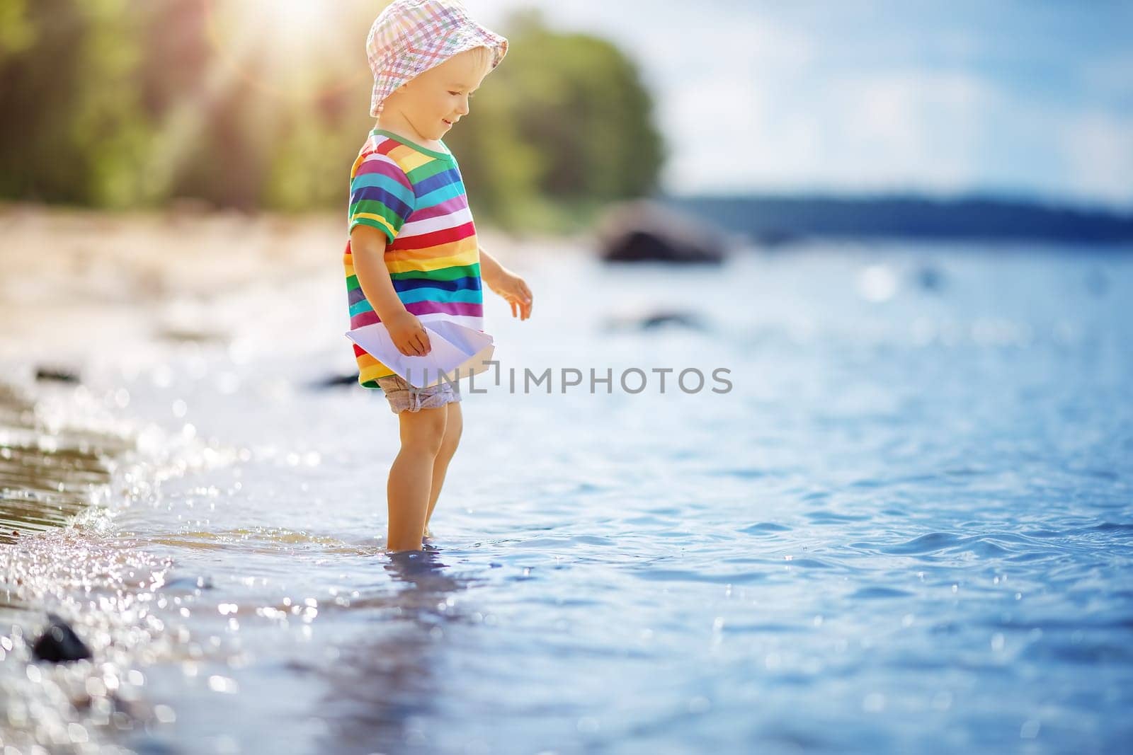 Cute boy playing with paper boat on the seashore. Concept of cruise and family vacation.