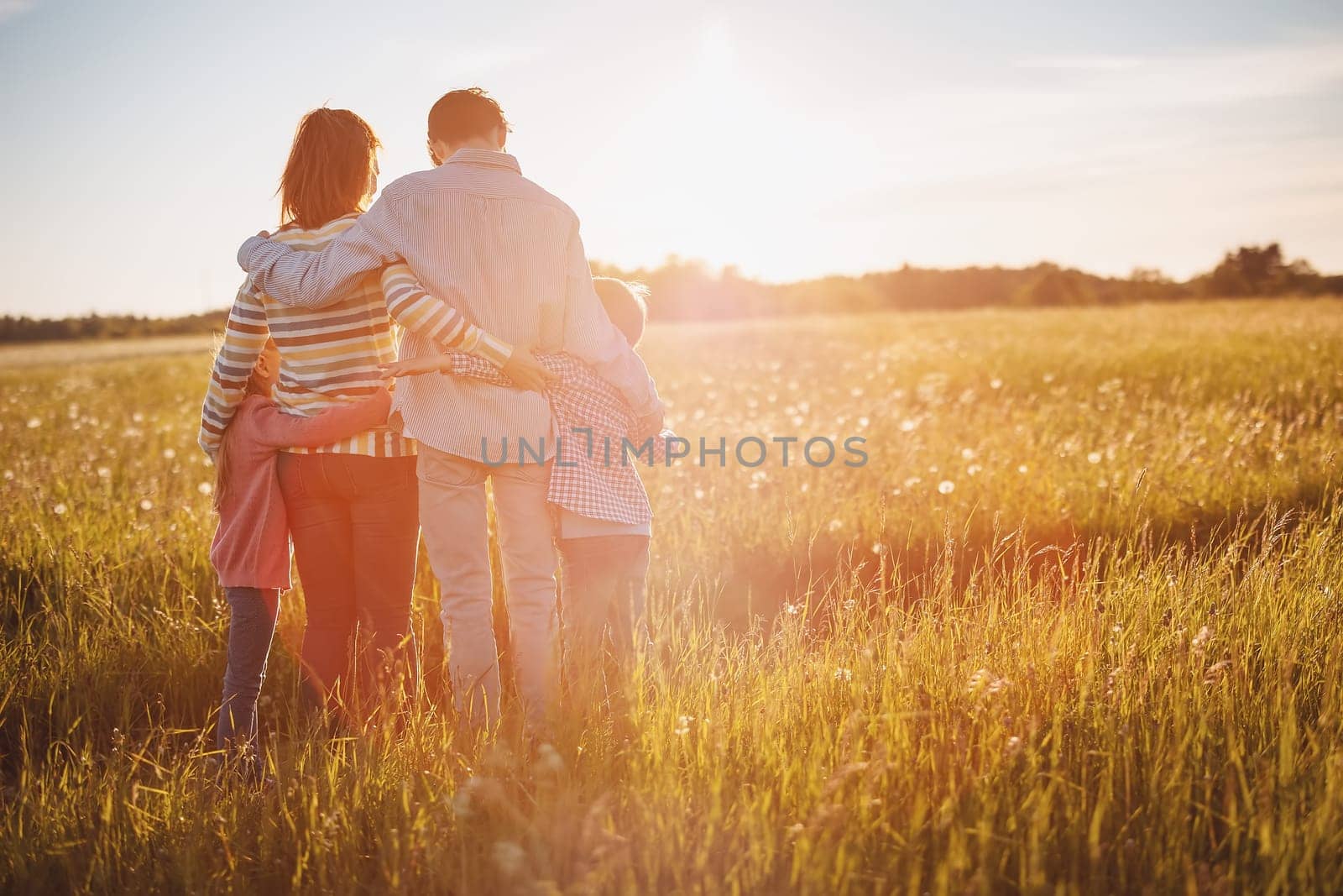 Happy family standing on the summer field and hugging on the sunset with love. Concept of the relation between people and vacation together.