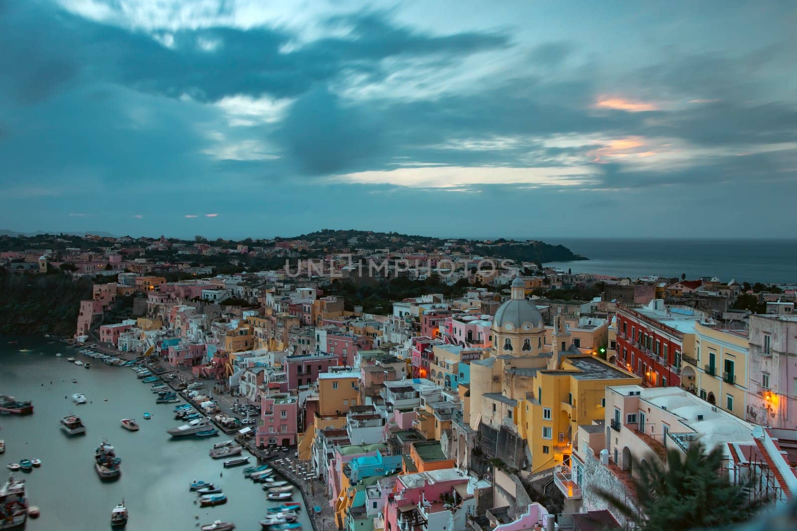 View of the Port of Corricella with lots of colorful houses after sunset in Procida Island, Italy.
