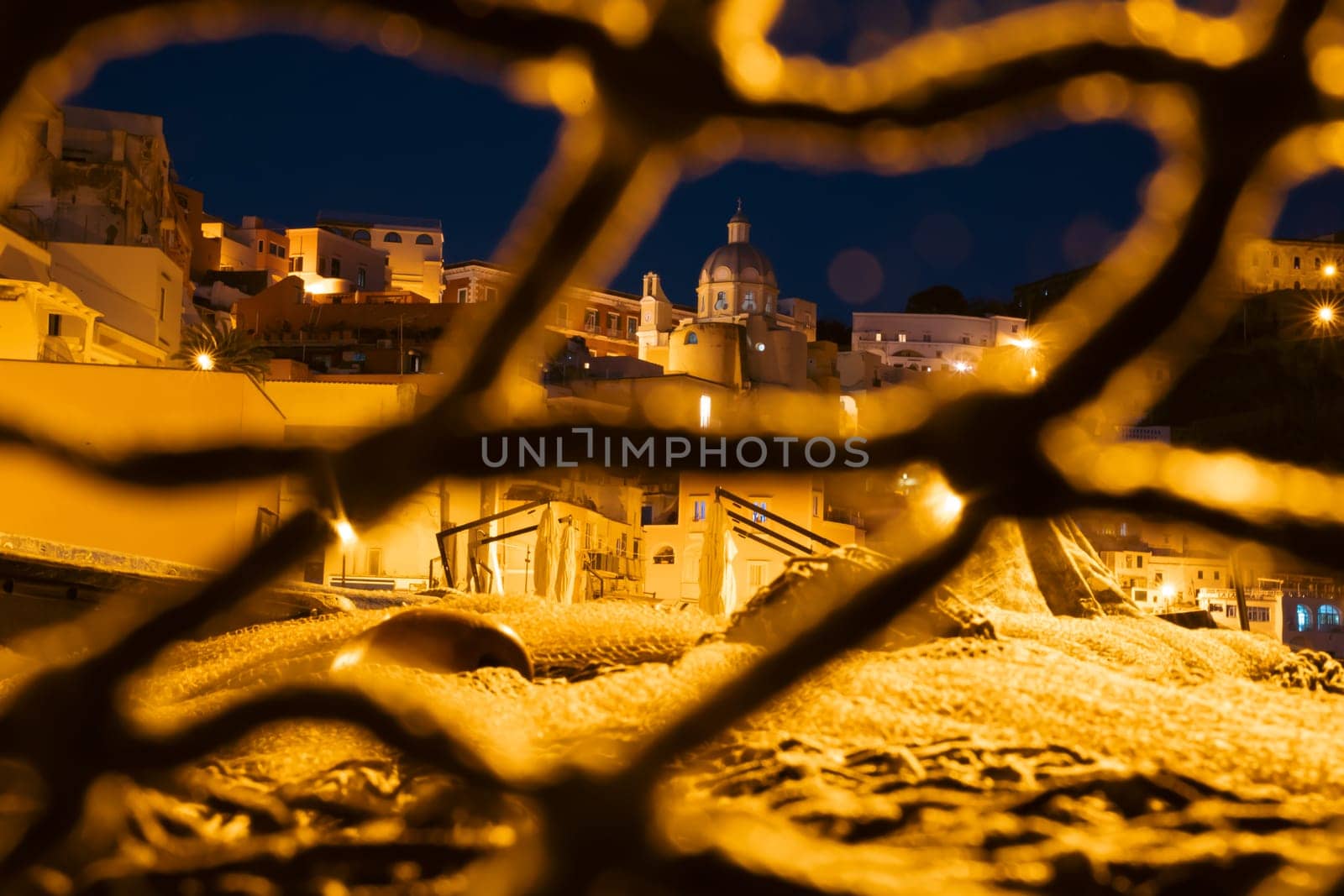 Fishing nets the Port of Corricella with lots of colorful houses after sunset in Procida Island, Italy.