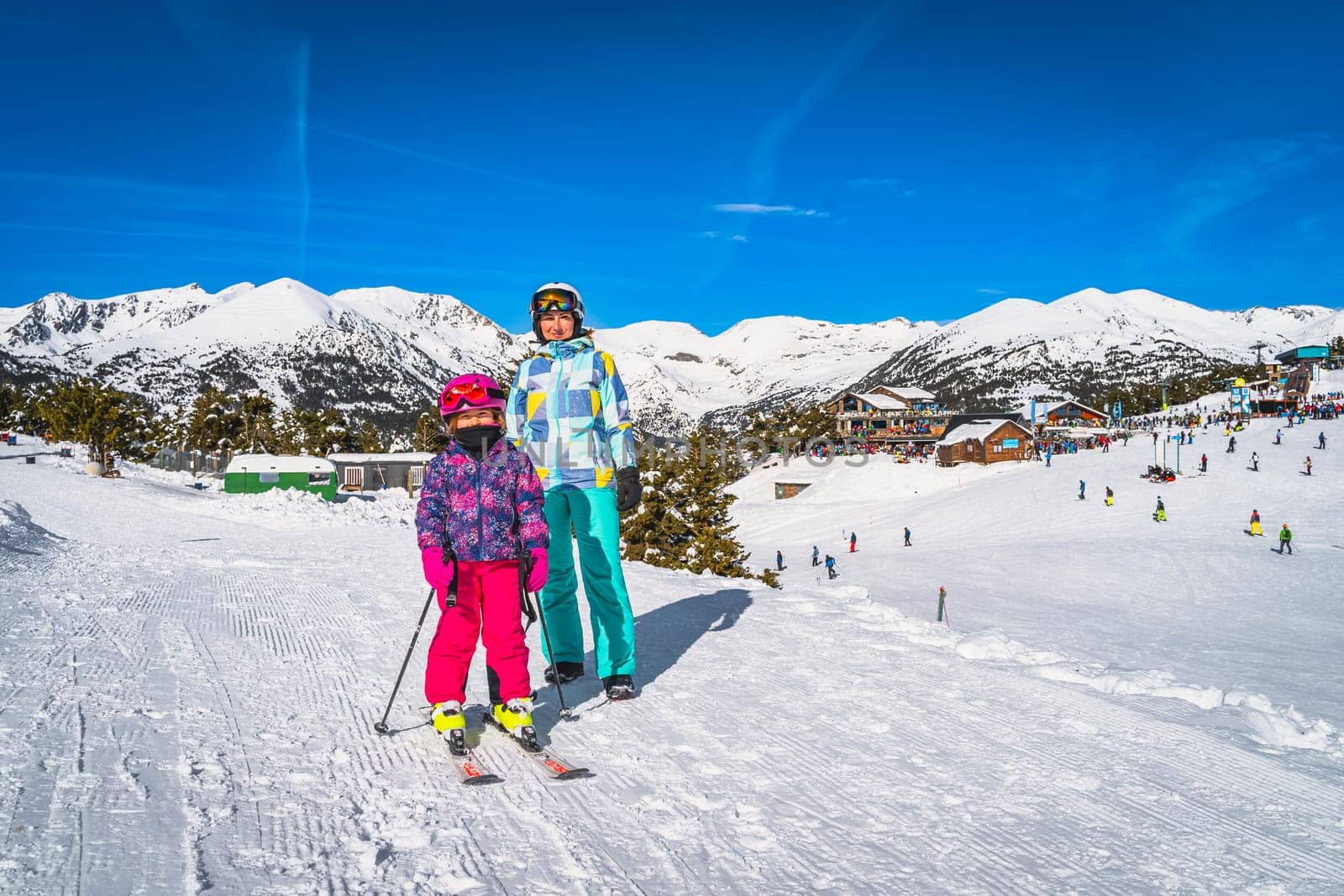 Mother and daughter, family, on ski, standing and smiling, ski resort, snow capped mountains and forest in background. Winter holidays, Andorra