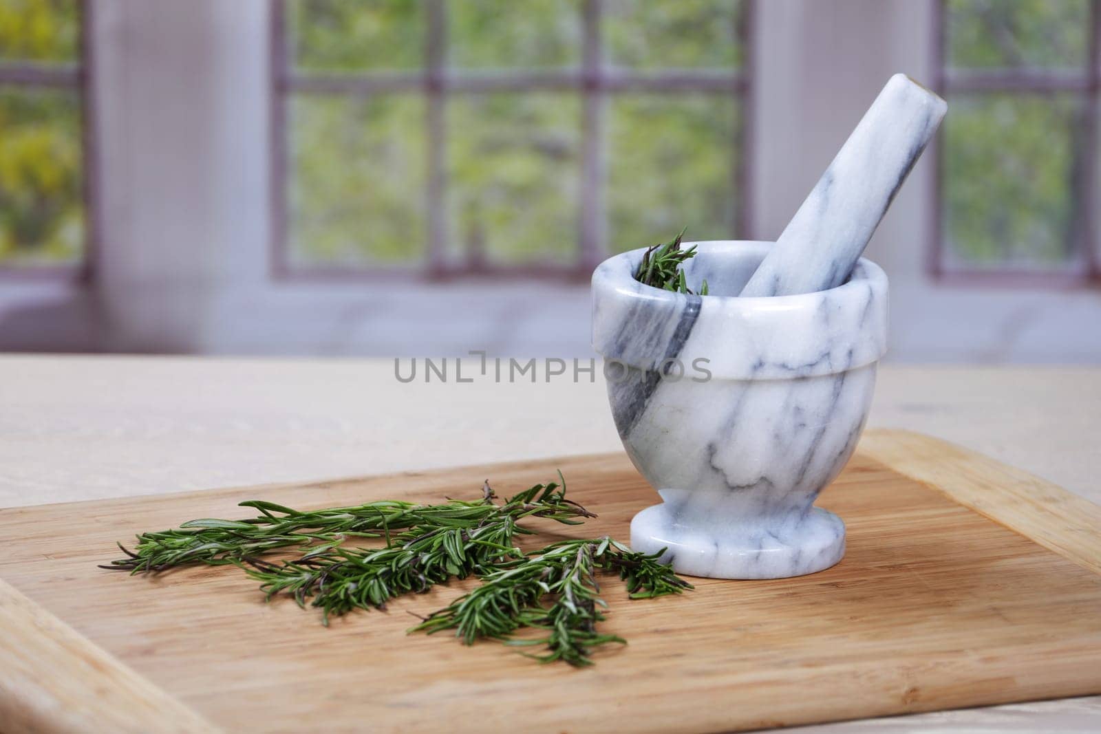 Rosemary herbs and a mortar and pestle on a wooden chopping board in a traditional kitchen