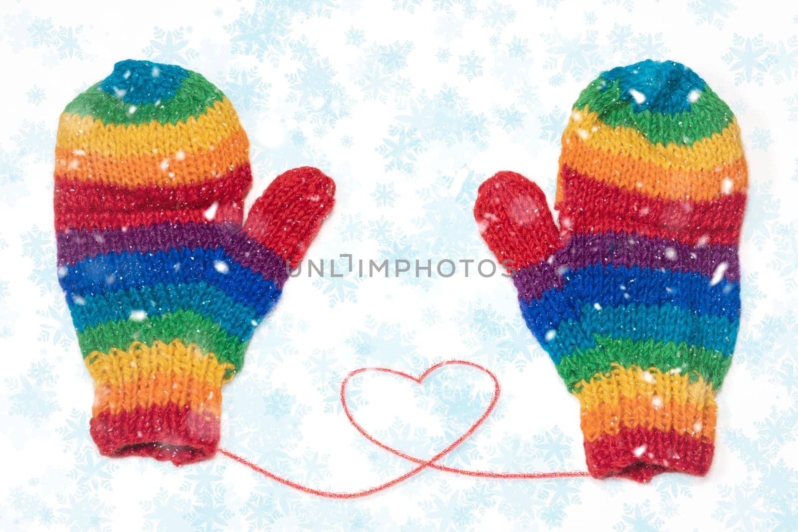 Rainbow colored gloves with a red heart while snowing in winter. Rainbow family.
