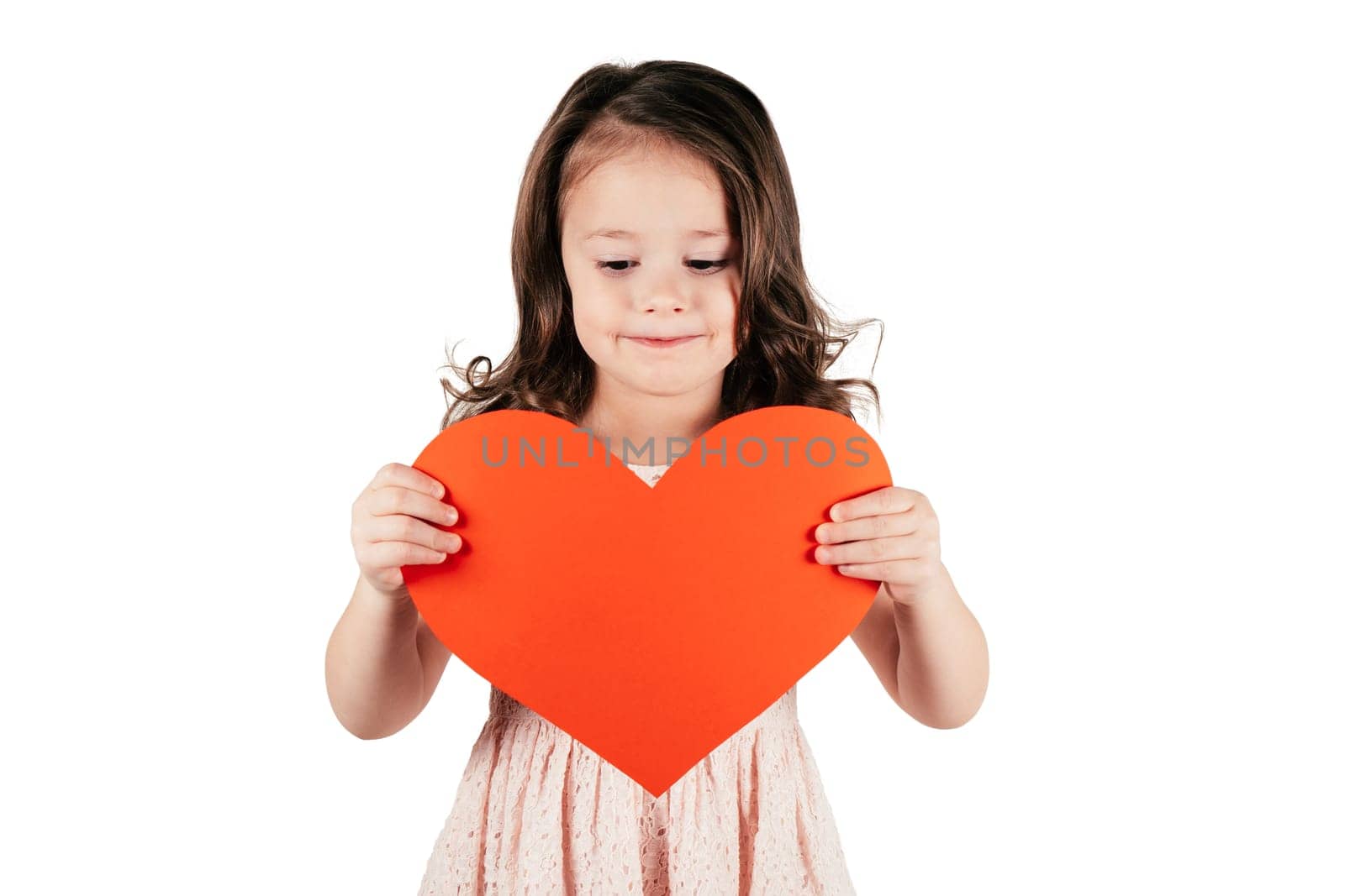 Portrait of little girl with curly hair hold in hands big red paper heart lowering eyes forcing smile isolated on white background. Family, love, holidays, birthday, Mother's day concept. Copy space