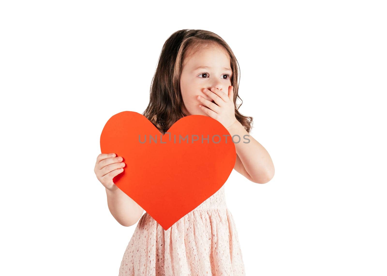 Portrait of little girl with long curly hair hold in hand red paper heart putting hand over mouth isolated on white background. Congratulations, Valentines day, birthday, Mother's day. Copy space