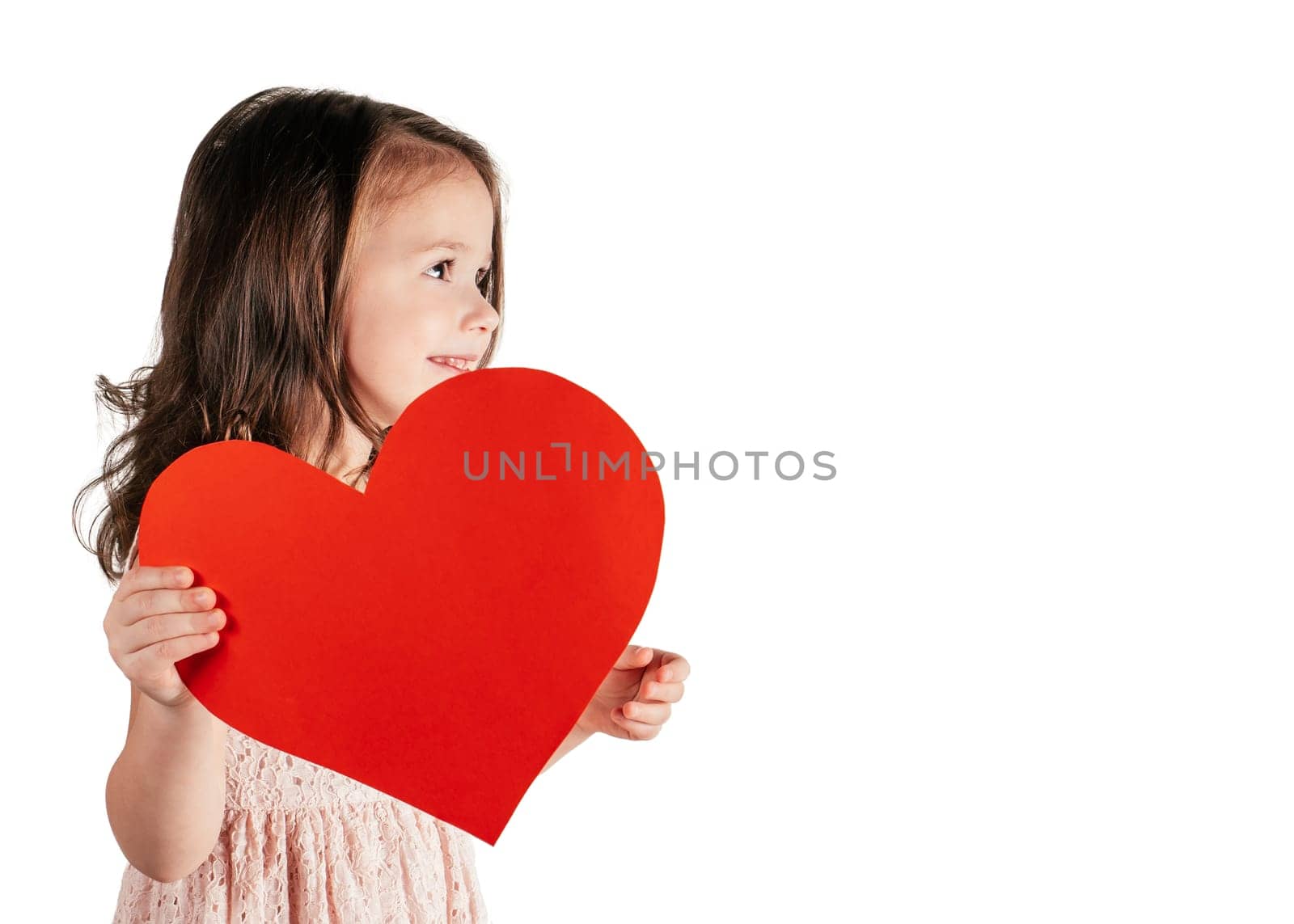 Portrait of little girl with long curly hair hold in hand big red paper heart isolated on white background. Family, love, birthday, Valentines day, Mother's day concept. Copy space, profile shot.
