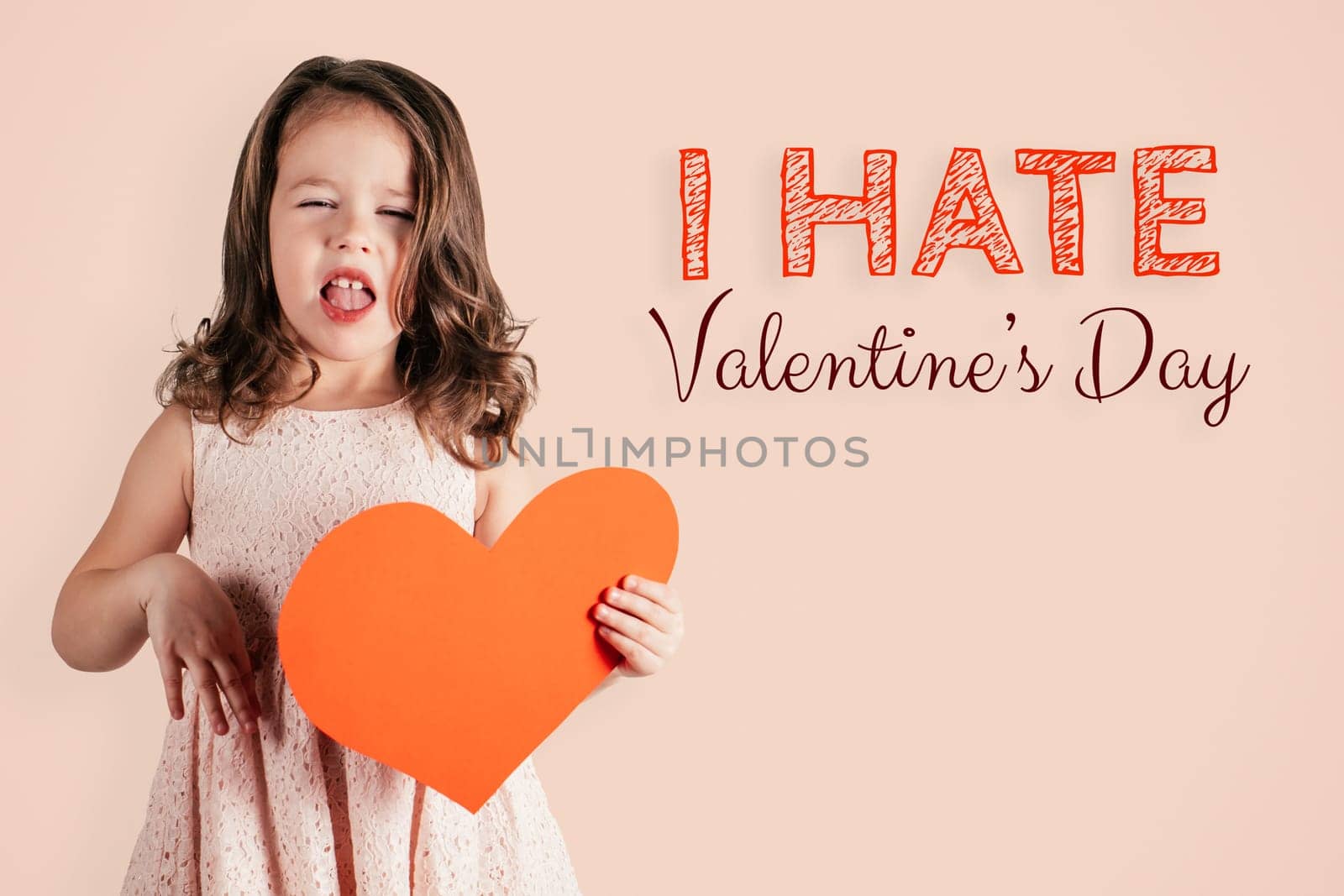 Portrait of little girl with long curly hair hold in hand big red paper heart showing disgust on peach background. Inscription I hate Valentines Day. Post or Greeting card. Copy space